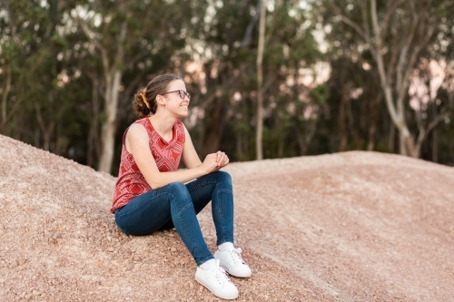 Young person sitting outside on dirt heap at dusk with bokeh light - Australian Stock Image