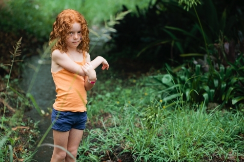 Young redhead girl standing in bushland holding her arm - Australian Stock Image