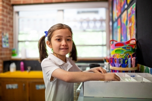 Young schoolgirl standing inside the classroom smiling at camer - Australian Stock Image