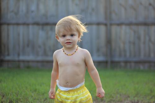 Young shirtless toddler playing in yard with wind blowing hair - Australian Stock Image