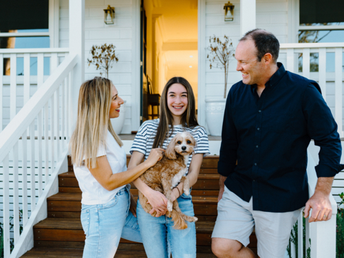 Young teenage girl carrying a dog while standing beside her parents outside the house. - Australian Stock Image