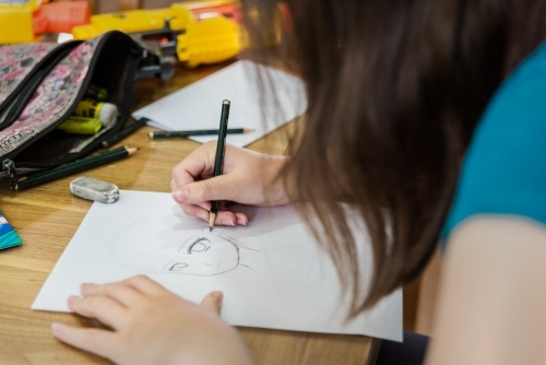 Young teenage girl creating artwork, drawing Manga and stencilling at the table - Australian Stock Image