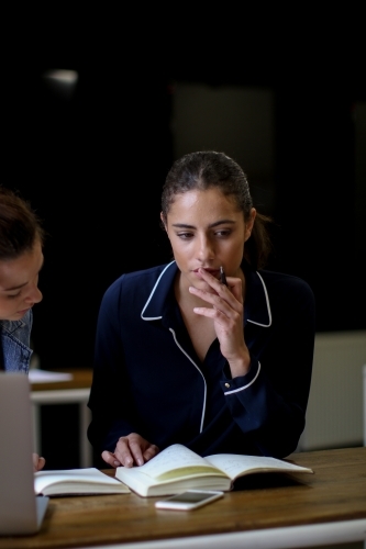 Young woman holding pen looking over notes with thoughtful expression - Australian Stock Image