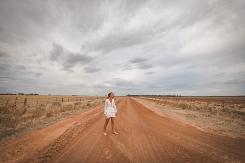 Young woman in white walking barefoot on rural dirt road - Australian Stock Image