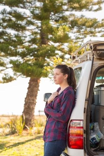 Young woman leaning against 4WD at seaside campground - Australian Stock Image