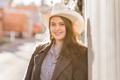 Young woman leaning against fence wearing hat smiling happy - Australian Stock Image