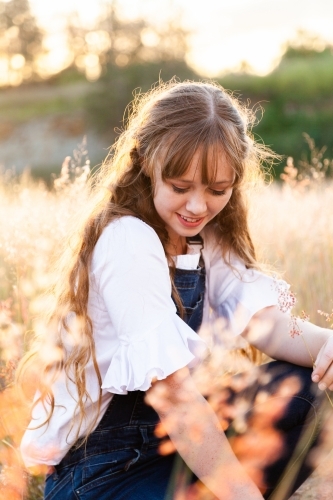 Young woman looking down smiling backlit by golden sunset light - Australian Stock Image