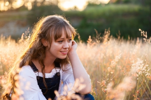 Young woman looking down smiling backlit by golden sunset light - Australian Stock Image