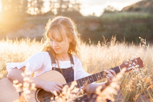 Young woman playing guitar in grass backlit by golden light