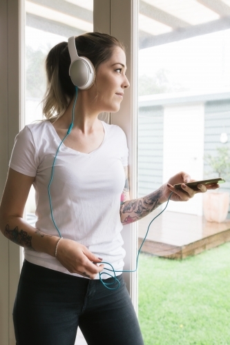 Young woman playing music on her phone looking out the window - Australian Stock Image