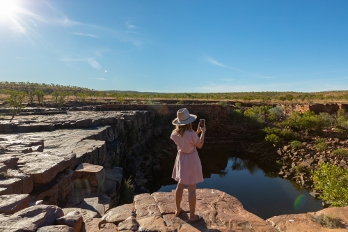 young woman seen from behind taking phone photo of landscape - Australian Stock Image