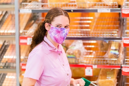 Young woman shopping for essentials like bread in grocery store during covid-19 pandemic - Australian Stock Image