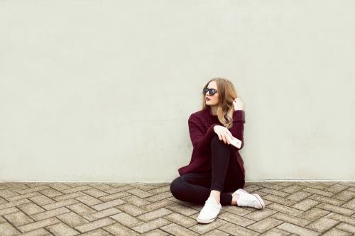 Young woman sitting against a wall with a phone and sunglasses - Australian Stock Image