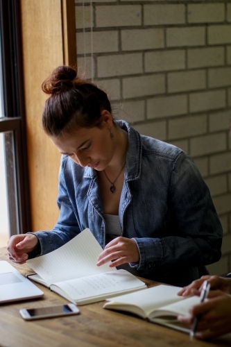 Young woman sitting at desk studying with books and laptop - Australian Stock Image