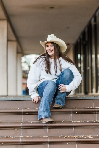 Young woman sitting at top of steps looking away hugging knee - Australian Stock Image