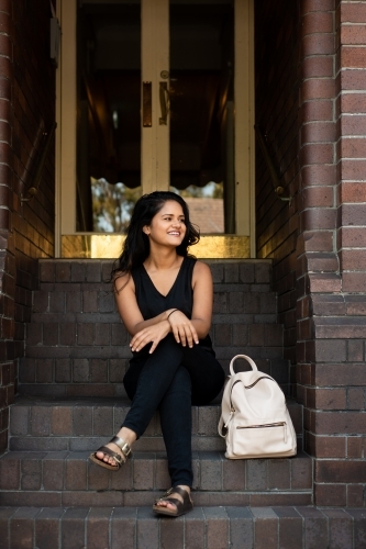 young woman sitting on stairs outside apartment entrance - Australian Stock Image