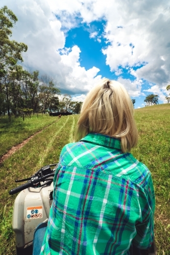 Young woman sitting on stationary quad bike watching dogs mustering cattle - Australian Stock Image