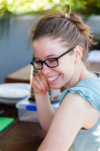 Young woman smiling over shoulder sitting at picnic bench - Australian Stock Image