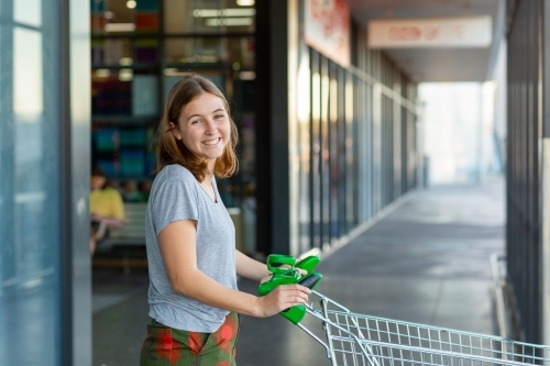 young woman smiling with shopping trolley at shops - Australian Stock Image