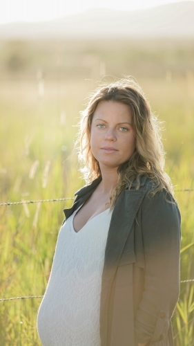 Young woman standing in field with sunflare behind - Australian Stock Image