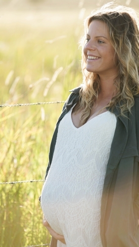 Young woman standing in field with sunflare behind, side profile - Australian Stock Image