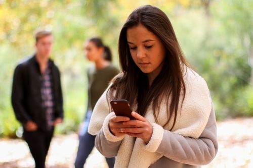 Young woman standing in front of a group of friends using a mobile phone - Australian Stock Image