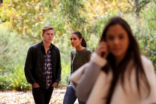 Young woman standing in front of a group of friends using a mobile phone - Australian Stock Image