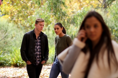 Young woman standing in front of a group of friends using a mobile phone - Australian Stock Image