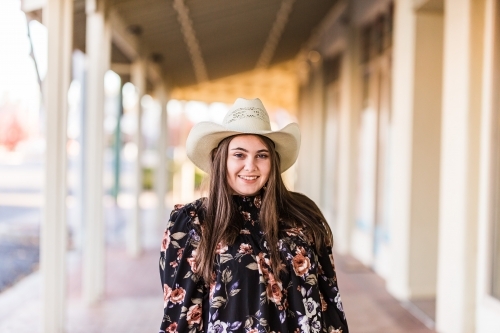 Young woman standing in main street wearing hat and floral shirt smiling - Australian Stock Image