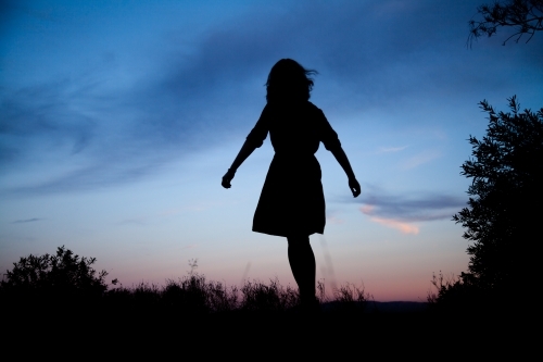 Young woman twirling silhouetted against pastel dusk sky - Australian Stock Image