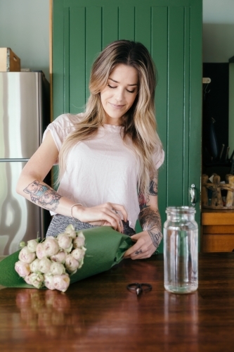 Young woman unwrapping fresh cut pink roses to place in a vase - Australian Stock Image