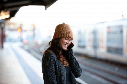 Young woman waiting at train station talking on mobile phone - Australian Stock Image