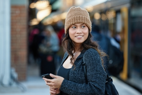 Young woman waiting at train station with mobile phone - Australian Stock Image