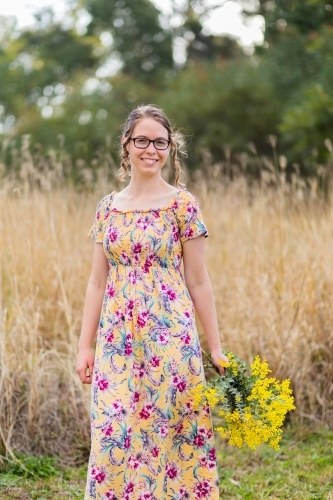 Young woman with bouquet of wattle blossoms outside in nature - Australian Stock Image