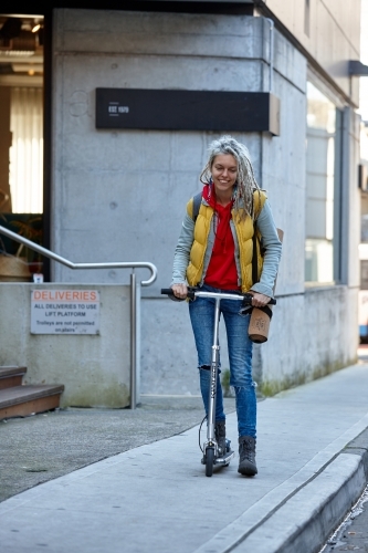 Young woman with dreadlocks riding electric scooter - Australian Stock Image