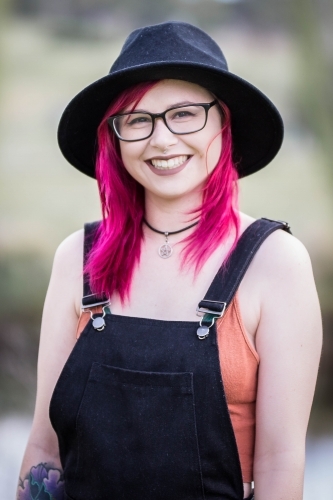 Young woman with pink hair glasses and hat smiling - Australian Stock Image