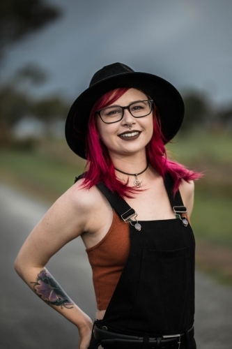 Young woman with pink hair hat glasses and tattoo smiling - Australian Stock Image